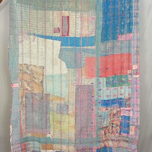 May include: A rectangular textile throw featuring a patchwork of various fabric panels in shades of blue, pink, yellow, and white. The surface is covered in dense, vertical running stitch patterns in contrasting thread colors throughout the piece.