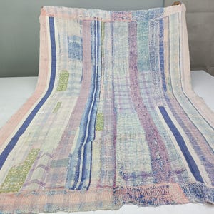 May include: A rectangular textile featuring a patchwork design with vertical stripes in shades of light pink, lavender, and blue. The fabric displays a visible running stitch pattern throughout, with small rectangular accents in lime green.