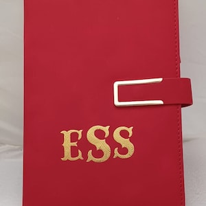 May include: Red leather journal with a gold metal clasp and the word "ESS" embossed in gold on the front cover.