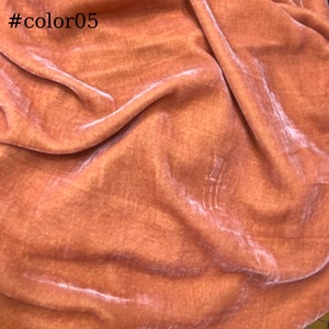 May include: A close-up of a peach-coloured fabric with a soft, velvety texture. The fabric is draped and folded, showing its smooth surface and subtle sheen.