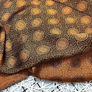 May include: Black fabric with a gold pattern of interlocking squares and circles. The fabric has a subtle sheen and a textured surface.