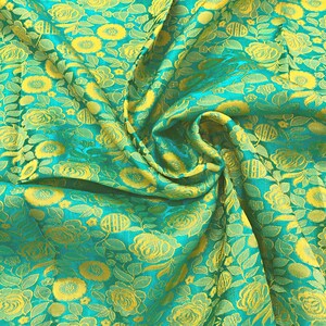 May include: A close-up of a teal fabric with a yellow floral pattern. The fabric is folded and draped, showing the texture and detail of the design.