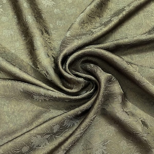 May include: A close-up of a textured, green fabric with a subtle sheen. The fabric is draped and folded, showcasing its soft, flowing texture.