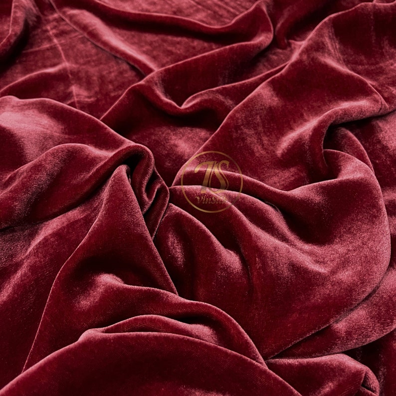 May include: Close-up of a deep red velvet fabric with a soft, luxurious texture. The fabric is draped and folded, creating a dramatic and elegant look.
