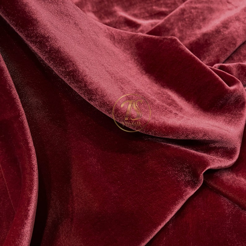 May include: Close-up of a deep red velvet fabric with a soft, plush texture. The fabric is folded and draped, showcasing its luxurious feel.