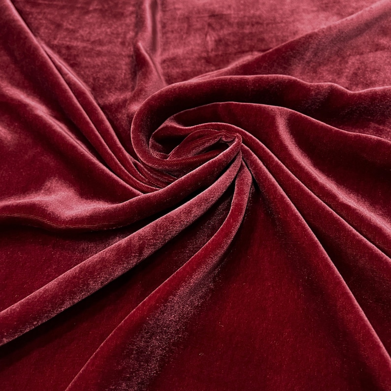May include: Close-up of a deep red velvet fabric with soft folds and a smooth texture.