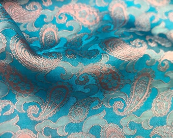 Pode incluir: Um tecido turquesa com um padrão paisley em um tom rosa mais claro. O tecido tem um brilho sutil e uma textura macia.