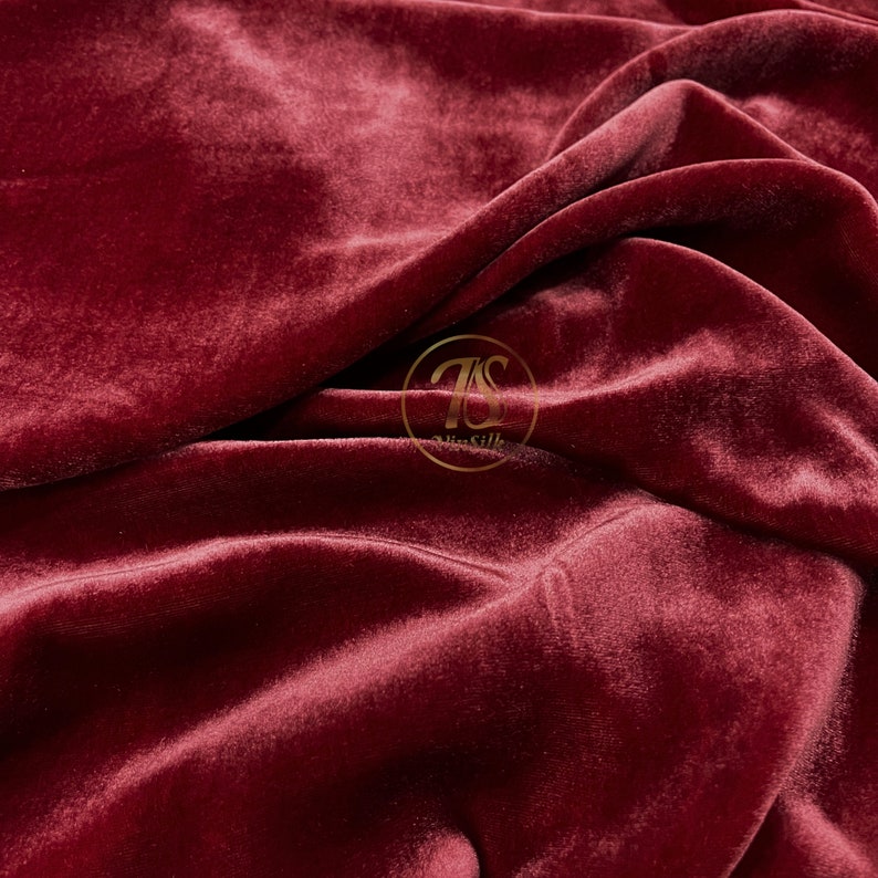 May include: Close-up of a deep red velvet fabric with a soft, plush texture. The fabric is draped and folded, creating a luxurious and elegant look.