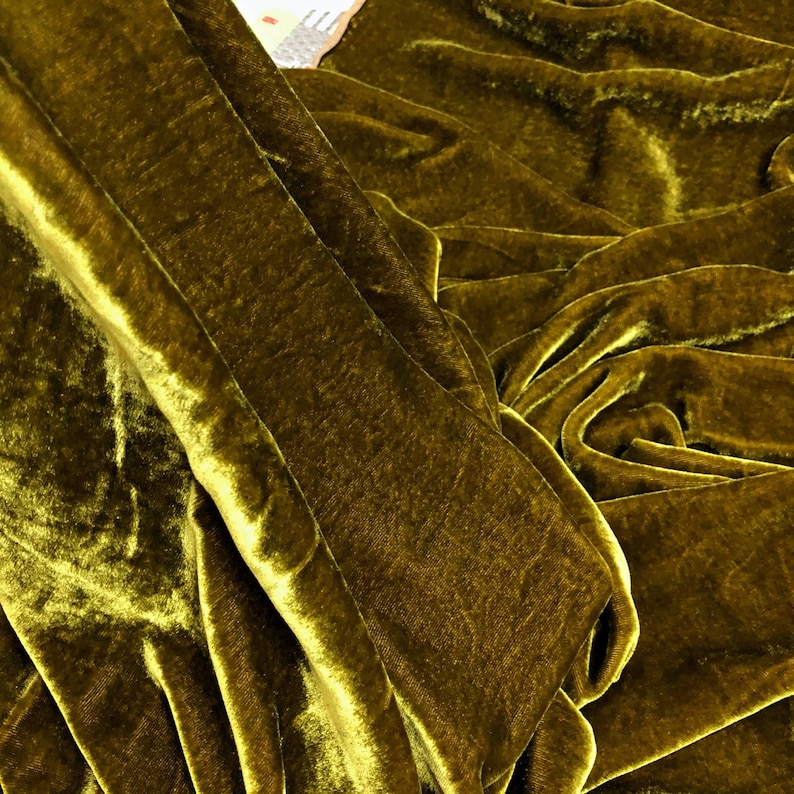 May include: Close-up of a deep green velvet fabric with a soft, plush texture. The fabric is folded and draped, showcasing its luxurious feel.