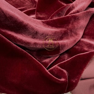 May include: Close-up of a deep red velvet fabric with a soft, plush texture. The fabric is folded and draped, showcasing its luxurious feel.