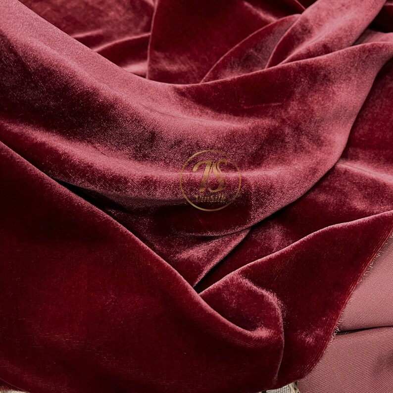 May include: Close-up of a deep red velvet fabric with a soft, plush texture. The fabric is folded and draped, showcasing its luxurious feel.
