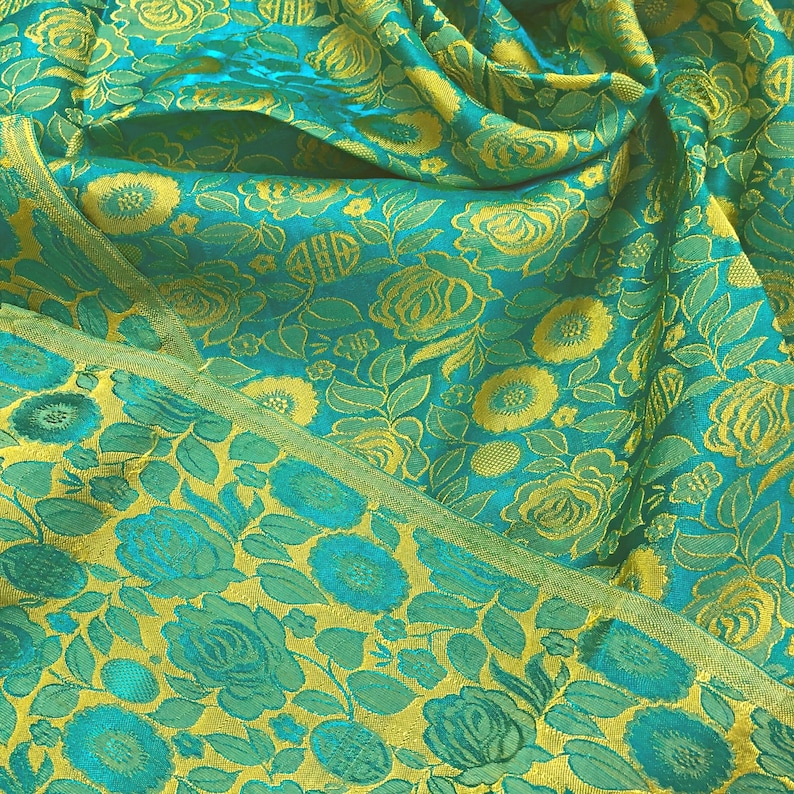 May include: A teal fabric with a yellow floral pattern. The fabric is folded and has a textured surface.