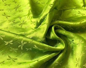 May include: Vibrant green fabric featuring a dragonfly motif. The material has a lustrous sheen and is arranged in flowing folds, producing shadows and highlights. The dragonfly pattern is a lighter green, providing a delicate texture.