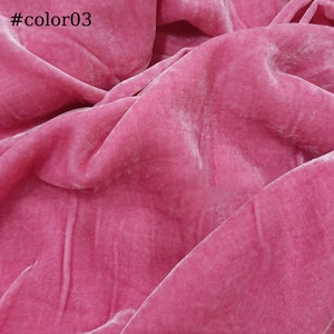 Puede incluir: Primer plano de una tela de terciopelo suave de color rosa. La tela tiene un brillo sutil y una superficie ligeramente texturizada.