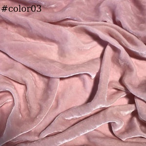 May include: A close-up of a soft, pink velvet fabric. The fabric is draped and folded, showing its texture and sheen.