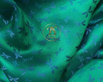May include: Emerald green fabric with a repeating pattern of blue dragonflies. The fabric has a subtle sheen, and the dragonflies are intricately detailed. The fabric is likely used for clothing or home decor.