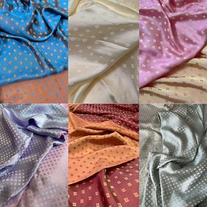 Op de afbeelding: Een collectie van zes stofstalen met een herhalend klein ruitpatroon. De kleuren zijn helderblauw, crème, lichtroze, lavendel, oranje en zilvergrijs. Elk stuk stof heeft een gladde, satijnachtige afwerking en textuur.