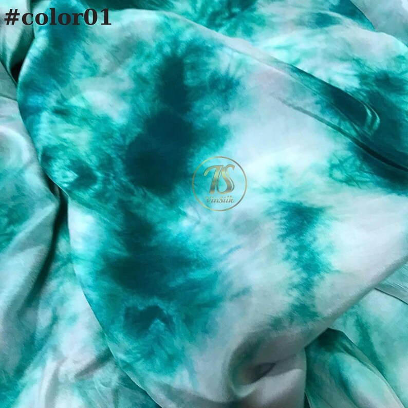 May include: A close-up of a teal and white tie-dye fabric. The fabric has a swirling pattern and is made of a soft, silky material.