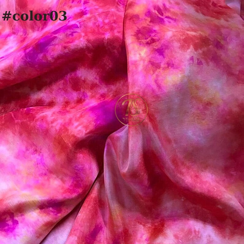 May include: A close-up of a pink, red, and yellow tie-dye fabric. The fabric has a soft, flowing texture and a vibrant, abstract pattern.