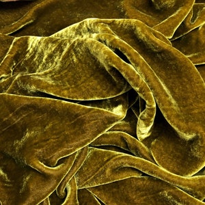 May include: Close-up of a soft, luxurious, olive green velvet fabric. The fabric is draped and folded, showcasing its texture and sheen.