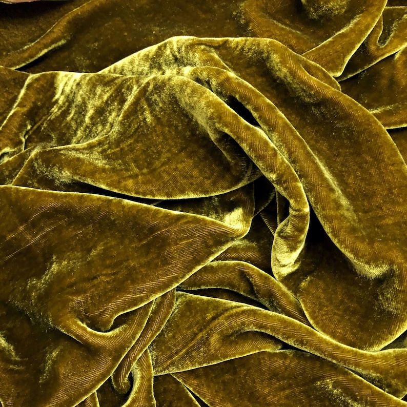 May include: Close-up of a soft, luxurious, olive green velvet fabric. The fabric is draped and folded, showcasing its texture and sheen.