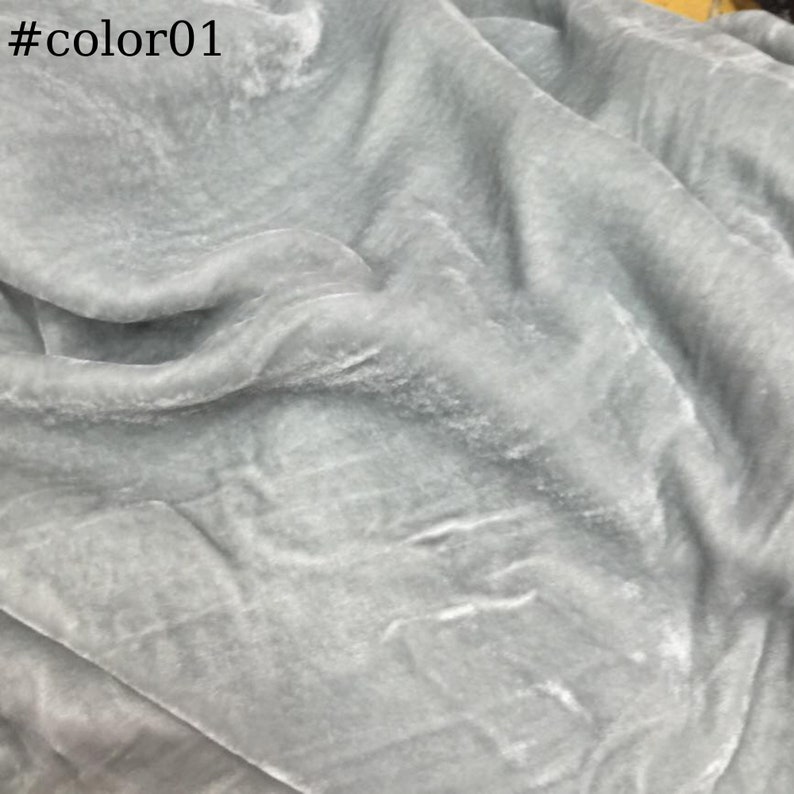 May include: A close-up of a light grey fabric with a soft, velvety texture. The fabric is wrinkled and has a subtle sheen.