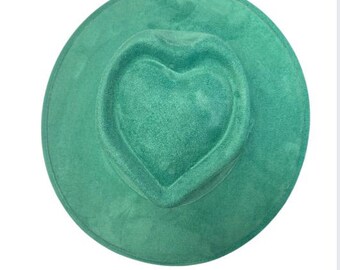 May include: A teal fedora-style hat with a heart-shaped crown. The hat has a wide brim and is made of a soft, velvety material. The hat is a solid teal color and is set against a white background.