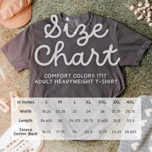 Pu&ograve; includere: Una maglietta grigio scuro Comfort Colors per adulti con una tabella delle taglie sovrapposta. La tabella mostra le misure in pollici per larghezza, lunghezza e centro manica posteriore per le taglie S-4XL. La maglietta &egrave; su una superficie strutturata.
