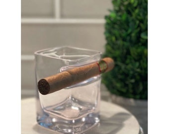 May include: A clear glass tumbler with a cigar holder built into the side. The glass is sitting on a white surface.
