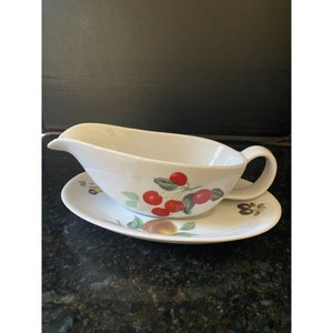 May include: White ceramic gravy boat with a handle and a matching saucer. Both pieces feature a cherry and peach design.