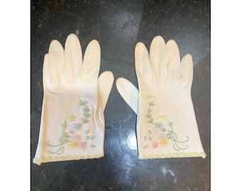 Puede incluir: Un par de guantes color crema con bordados florales. Los guantes presentan un delicado diseño de flores bordadas en colores pastel, con un borde festoneado. Los guantes son probablemente vintage o antiguos.