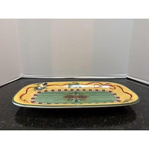 May include: Rectangular serving tray with a festive Christmas theme. The tray features a yellow border with red ribbon and green accents. The center has a green background with a pinecone design. The tray is made of ceramic.