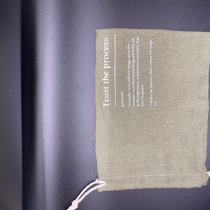 May include: A green fabric pouch with a white drawstring. The pouch has the text "Trust the process" printed on it, with the definition of the word "patience" underneath.