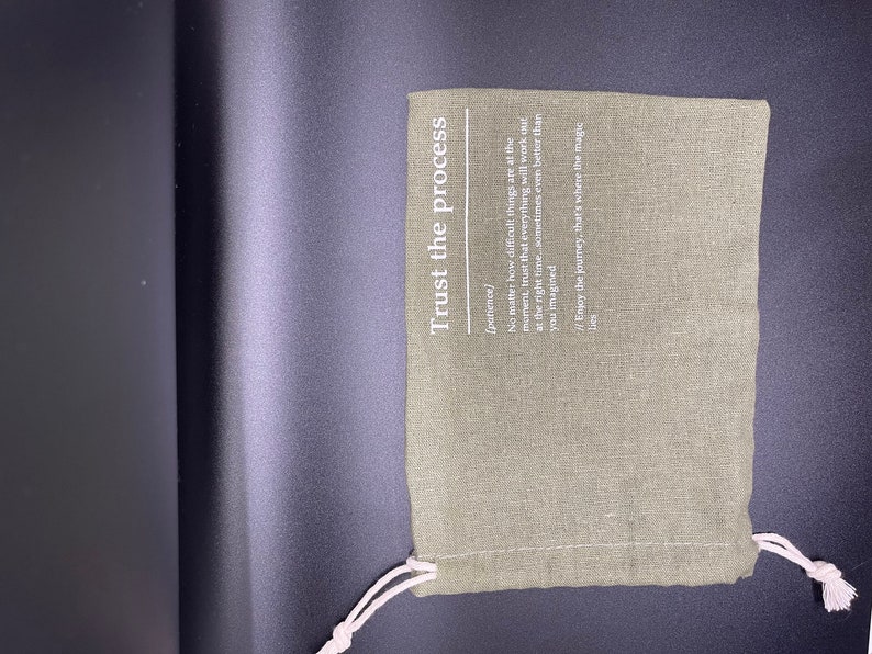 May include: A green fabric pouch with a white drawstring. The pouch has the text "Trust the process" printed on it, with the definition of the word "patience" underneath.