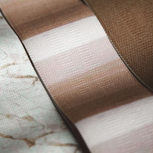 May include: Three different fabric ribbons with different patterns. The first ribbon is white with a brown marble pattern. The second ribbon is brown and white striped. The third ribbon is solid brown.