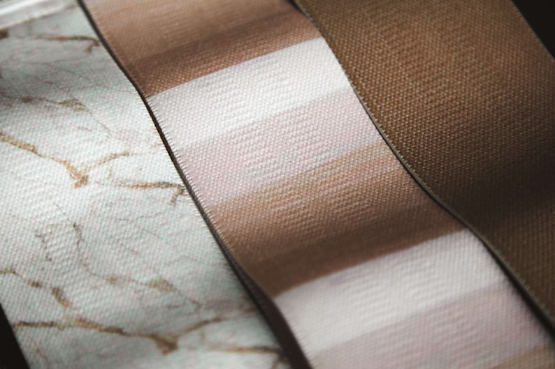 May include: Three different fabric ribbons with different patterns. The first ribbon is white with a brown marble pattern. The second ribbon is brown and white striped. The third ribbon is solid brown.