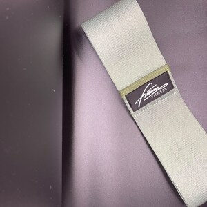 May include: A light gray fabric resistance band with a black label that says "Fitline Fitness".