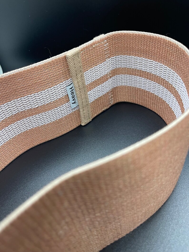 May include: A brown fabric resistance band with two white stripes and the word "Heavy" printed on it.