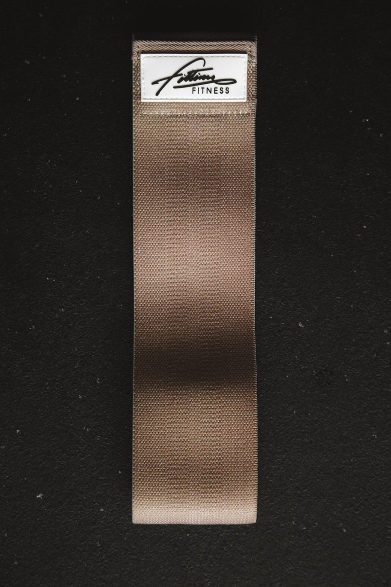 May include: A brown fabric resistance band with a white label that says "Fitness" in black text.