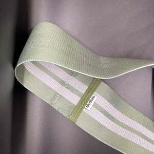 May include: A green exercise resistance band with two white stripes. The band is labeled "Medium".