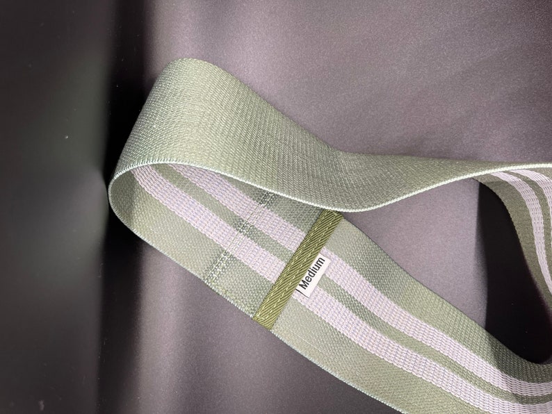 May include: A green exercise resistance band with two white stripes. The band is labeled "Medium".