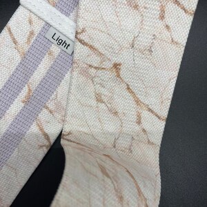 May include: White fabric resistance band with a marble print and a light gray stripe. The band has the word "Light" printed on it.