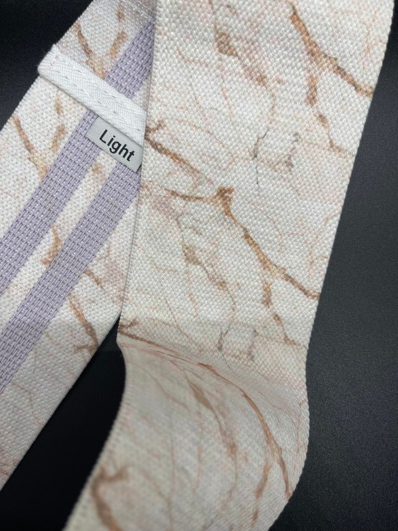 May include: White fabric resistance band with a marble print and a light gray stripe. The band has the word "Light" printed on it.