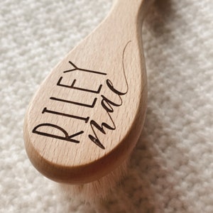 May include: A wooden hair brush with a natural bristle brush head. The handle is engraved with the name "Riley Mae".