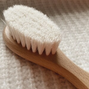 May include: A close-up of a wooden brush with white bristles. The brush is lying on a white fuzzy surface.