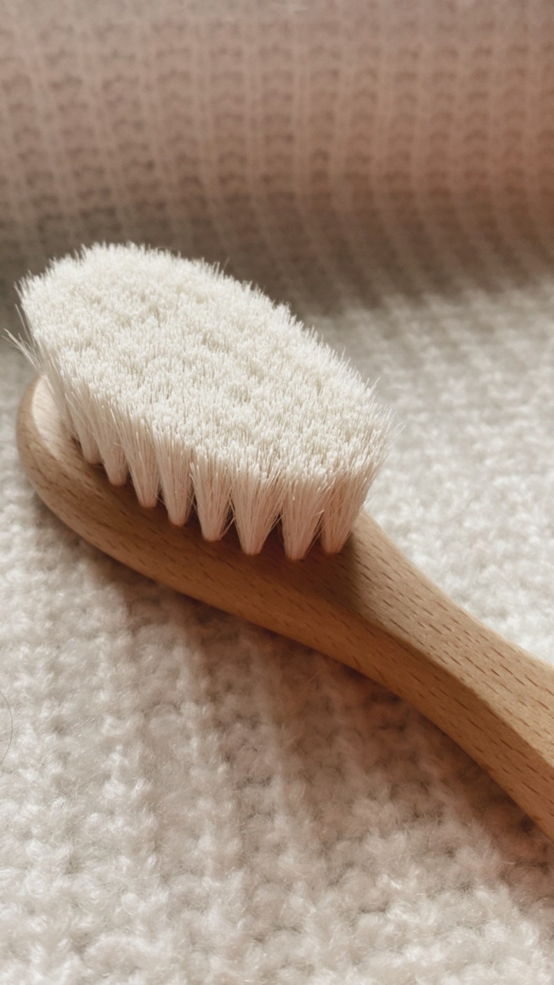 May include: A close-up of a wooden brush with white bristles. The brush is lying on a white fuzzy surface.