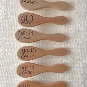 May include: Six wooden hairbrushes with personalized names engraved on them. The names are Moses, Riley Mae, Madelyn Louise, Jennifer Lea, Evelyn Claire, and Chapel May.