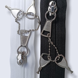 Puede incluir: Dos tiradores de cremallera con deslizadores de cremallera en forma de llave. Un tirador de cremallera es blanco y el otro es negro.