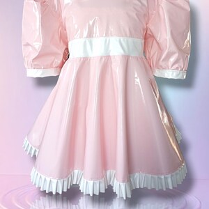 May include: A pink dress featuring a white Peter Pan collar, short puffed sleeves, and a white waistband. The dress has a full skirt with a white ruffled hem. The shiny material reflects light.