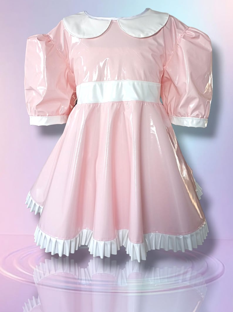 May include: A pink dress featuring a white Peter Pan collar, short puffed sleeves, and a white waistband. The dress has a full skirt with a white ruffled hem. The shiny material reflects light.